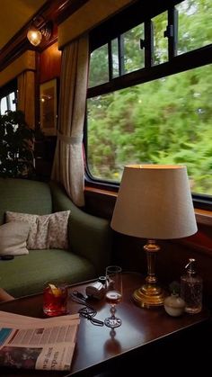 a green couch sitting next to a window on top of a wooden table near a lamp