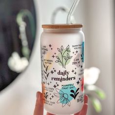 a hand holding a glass jar with a straw in it that says daily reminders