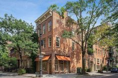 an old brick building on the corner of a street with lots of trees in front of it