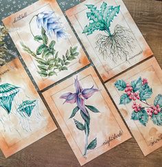 four cards with flowers and leaves on them sitting on top of a wooden table next to a plant