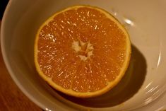 an orange sitting in a white bowl on top of a wooden table