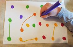 a child's hand holding a pencil over a paper with colored dots on it