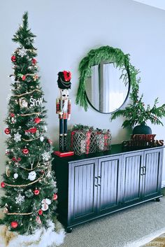 a christmas tree sitting next to a dresser with ornaments on it and a wreath hanging from the wall