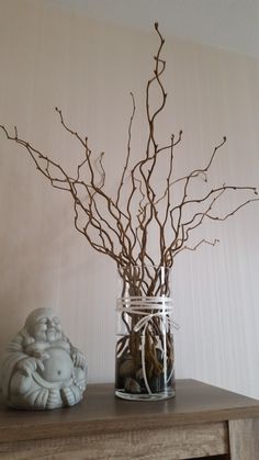 there is a vase with branches in it on the table next to a small figurine