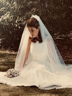 a woman in a wedding dress sitting on the grass with her veil over her face