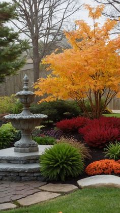 a stone fountain surrounded by colorful flowers and trees in the back yard with fall foliage