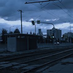 an empty train track with traffic lights and buildings in the background at dusk, as dark clouds loom overhead