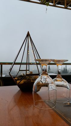 two wine glasses sitting on top of a wooden table next to a vase and candle holder