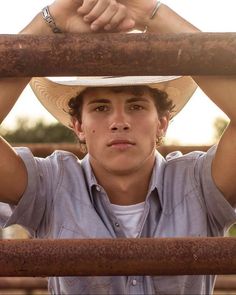 a young man wearing a cowboy hat and holding his hands over the top of his head