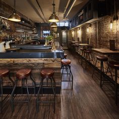 an empty bar with stools and wooden tables in the center, along with brick walls