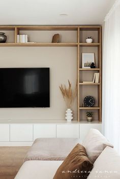 a flat screen tv mounted on the wall in a living room with white walls and wooden shelves