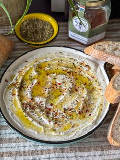 a bowl of hummus with bread and seasoning next to it on a table