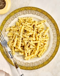 a white plate topped with macaroni and cheese next to a fork on top of a table