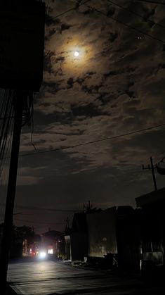 the moon is shining brightly in the night sky over an empty street with power lines and telephone poles