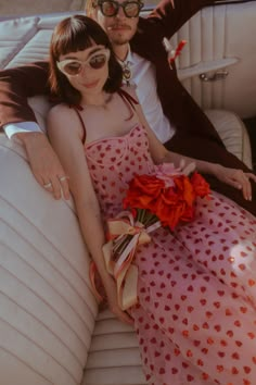 a man and woman sitting on the back of a car with flowers in their lap