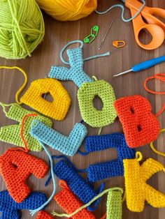 crocheted letters and yarn on a table with scissors, knitting needles and balls of yarn