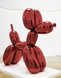 a red balloon dog sculpture sitting on top of a wooden floor next to a white wall