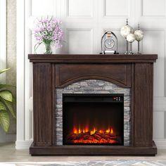 an electric fireplace in a living room with a clock on the mantle and flowers next to it