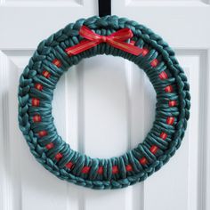 a knitted wreath hanging on a white door with red ribbon and bow around it