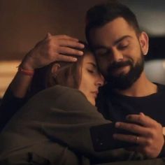 a man and woman cuddle together while looking at a cell phone in the dark