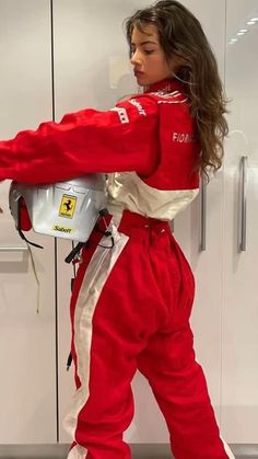 a woman in red and white racing suit standing next to a locker with her helmet on