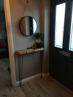 a mirror hanging on the wall next to a wooden table with hairpin legs and a potted plant