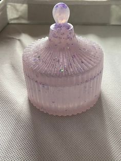 a pink glass container sitting on top of a white cloth covered table next to a window