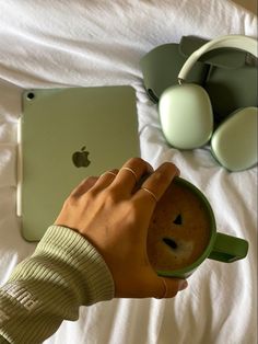 a person is holding a cup in their hand while using an apple laptop on the bed