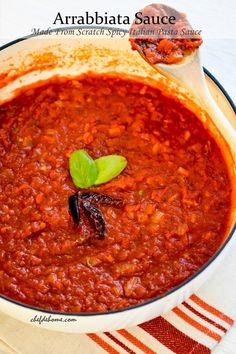 a bowl filled with red sauce and bread on top of a white table topped with a green leaf