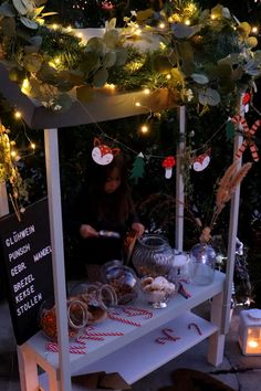 a woman standing at a table with food on it and lights strung up above her