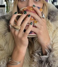 a woman in a fur coat drinking from a coffee cup with rings on her fingers