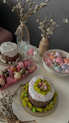 there are several cakes on the table with eggs and flowers in vases next to them