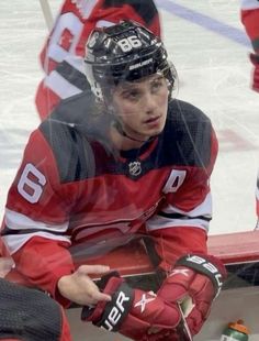 a hockey player sitting on the bench with his hands in his pockets and wearing gloves