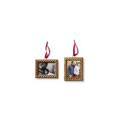 two framed pictures hanging from red ribbon on white wall next to each other with an ornament in the middle