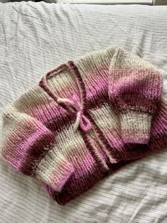 a pink and white sweater laying on top of a bed