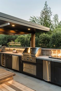 an outdoor kitchen with stainless steel grills and fire pit in the middle of it