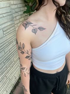 a woman with a tattoo on her arm and shoulder is standing in front of a brick wall