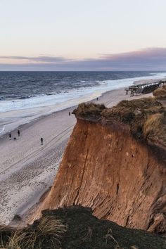 people are walking on the beach next to a large cliff that has been cut down