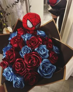 a bouquet of red and blue roses with a spiderman hat on top in a cardboard box