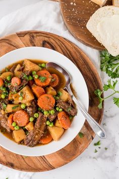 a white bowl filled with stew and carrots on top of a wooden cutting board