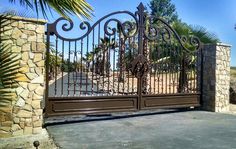 an iron gate with stone pillars and palm trees in the background