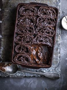 a chocolate cake sitting on top of a metal tray next to a spoon and cup