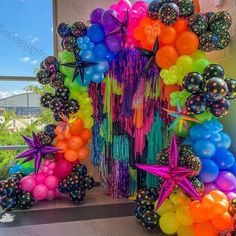 an assortment of balloons and streamers are arranged in the shape of a rainbow arch