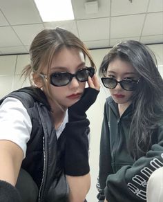 two young women wearing black sunglasses are taking a selfie in an office cubicle