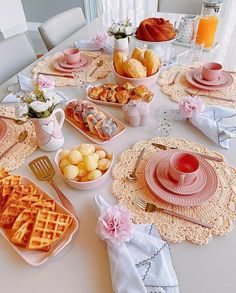 a white table topped with pink plates and bowls filled with food on top of it