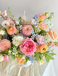 a vase filled with lots of colorful flowers on top of a white cloth covered table