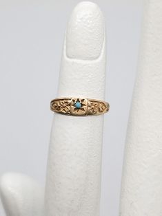 a gold ring with a blue stone in the middle on a white finger, against a plain background