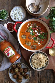 a bowl of soup with meatballs, rice and sauce next to other dishes on a wooden table