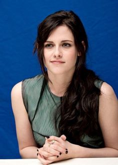 a woman sitting at a table in front of a blue background with her hands folded