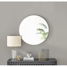 a round mirror sitting on top of a table next to a lamp and a vase